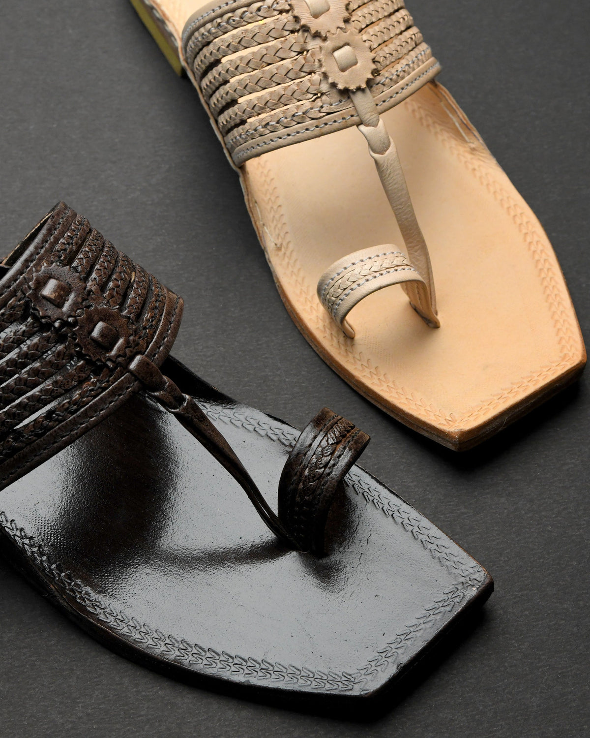 Close-up of a black sandal and a beige sandal on a dark background