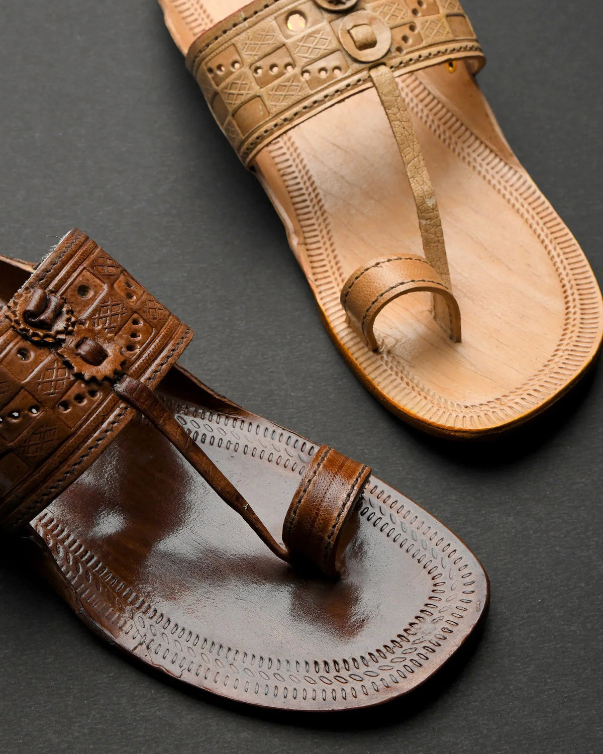 Pair of brown leather sandals with intricate designs on a dark background