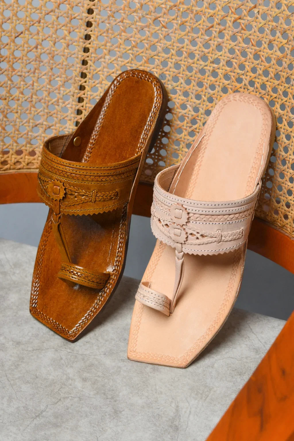 Pair of brown and beige sandals on a textured surface with wicker chair background